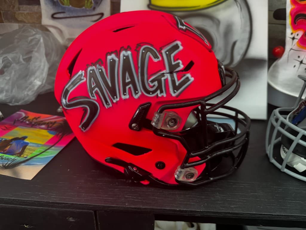 Custom airbrushed neon pink football helmet with Savage lettering